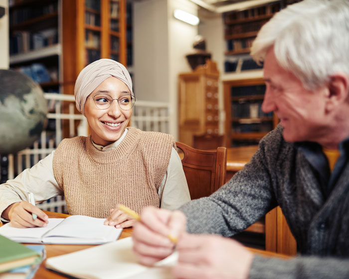 Eine junge Frau und ein älterer Herr sitzen an einem Tisch und bearbeiten Deutsch-Aufgaben