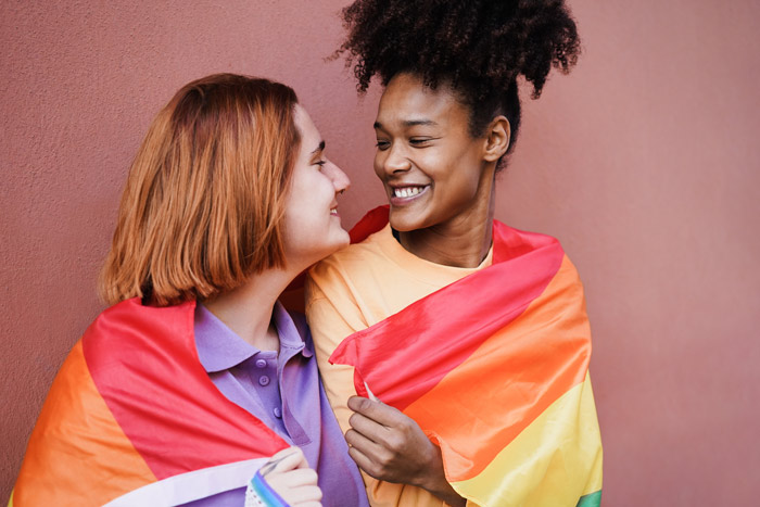 Zwei Frauen unter einer LGBTQ-Fahne lächeln sich an