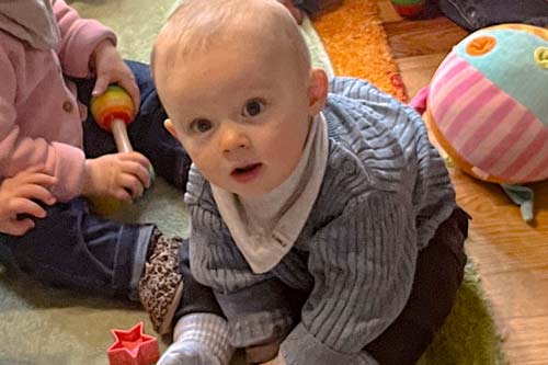 Ein Baby sitzt auf einem Teppich und schaut in die Kamera