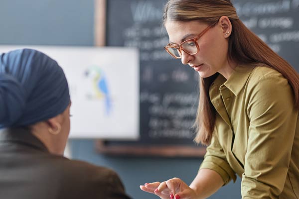 Eine Frau vor einer Tafel erklärt einer sitzenden Frau etwas