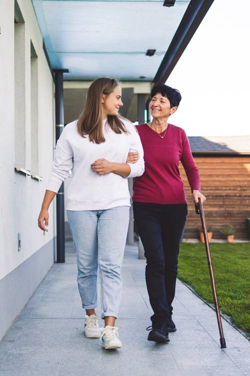 Eine junge Frau hakt eine ältere Frau am Stock ein und läuft auf die Kamera zu